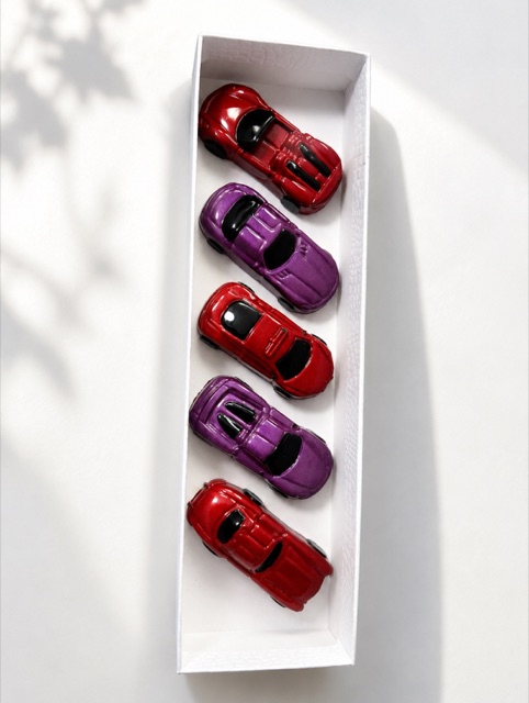 All five glossy red and purple car-shaped chocolates in a long white gift box