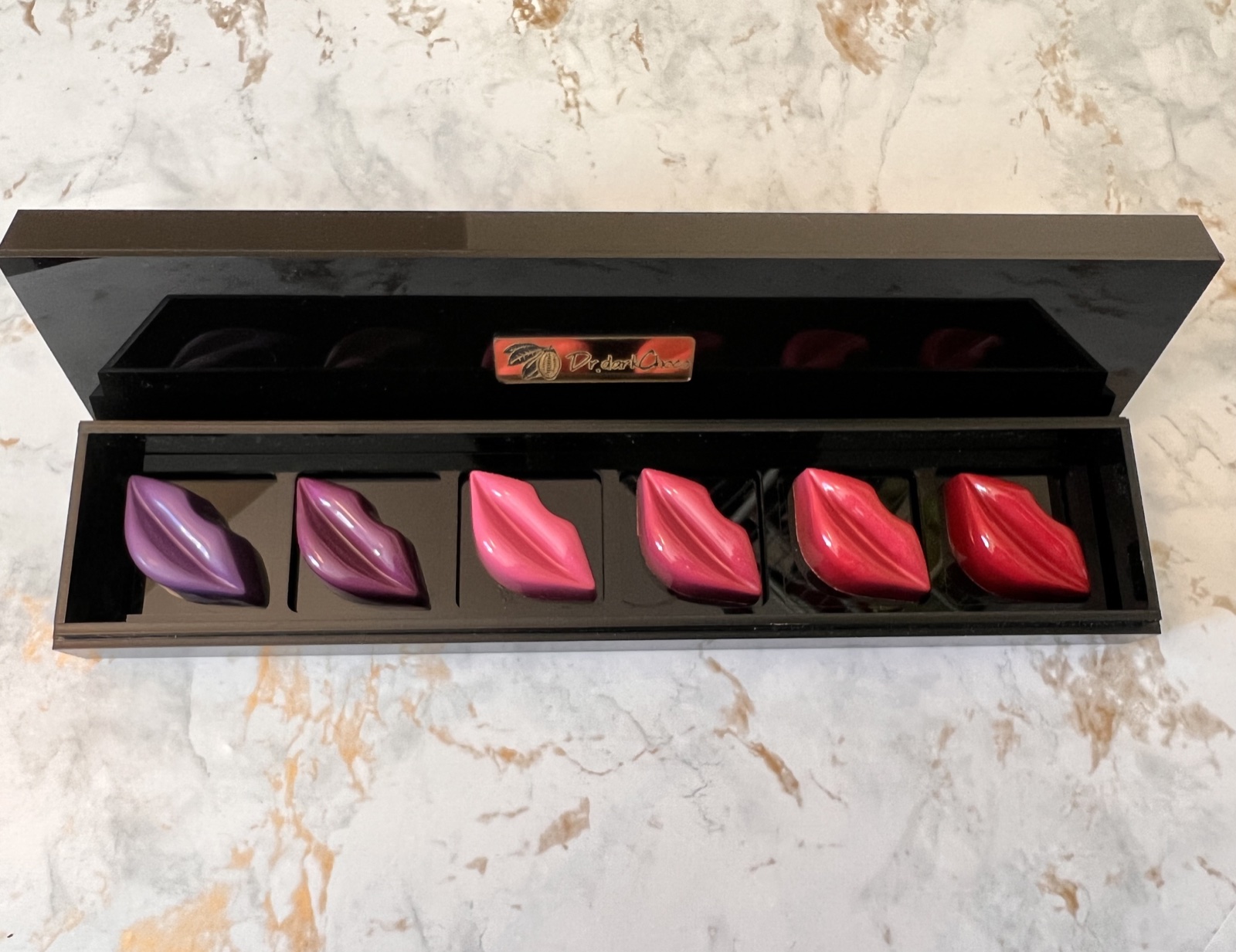 Open black Dr.darkChoco box holding all six purple, pink and red lip-shaped chocolates