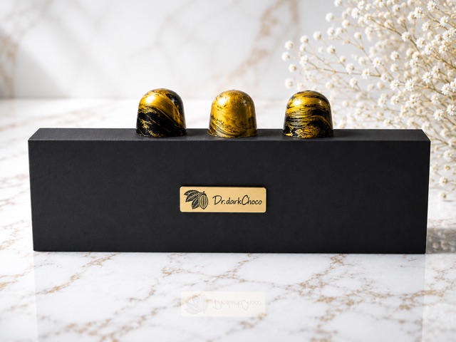 Three gold-painted pralines arranged on a black Dr.darkChoco gift box